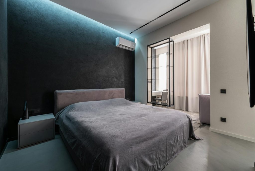 Interior design of contemporary spacious bedroom with comfortable soft bed with bedside table and air conditioner in apartment